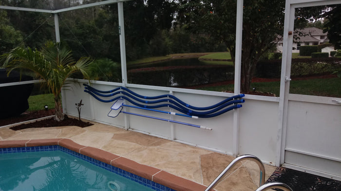 Pool sweep hoses hung along enclosure kick-plate rail on hooks.