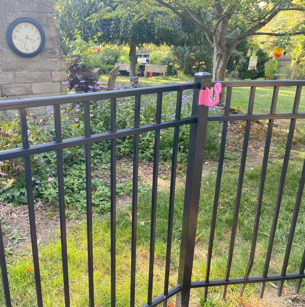 Garden with clock, metal fence, and pink flamingo.