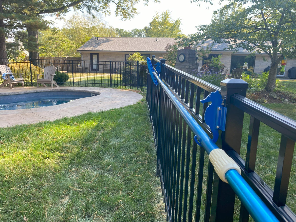 Blue pool pole on two blue clamp-on hooks on black aluminum fence.