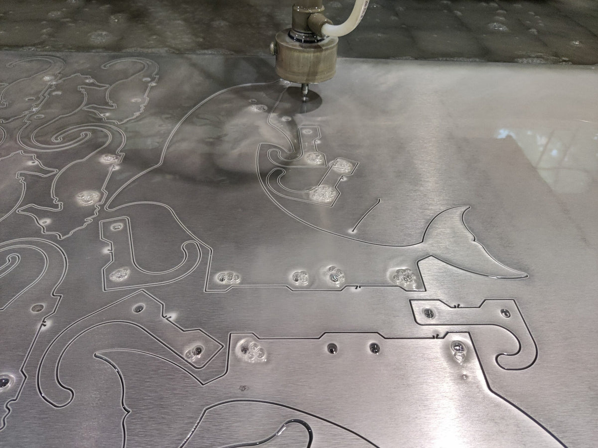 Waterjet cutting shapes in aluminum sheet at Akron workshop.