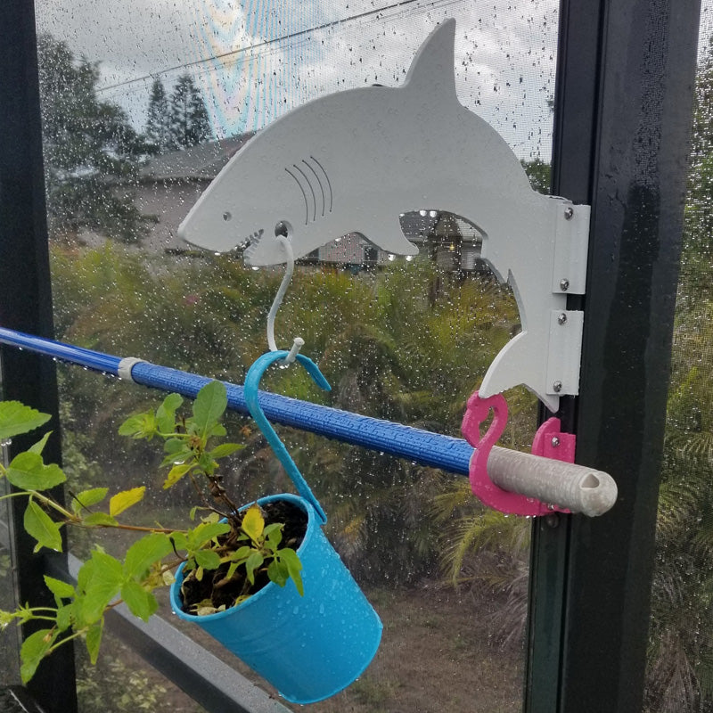 Silver shark hanger holding blue planter on a lanai post.