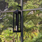 Outdoor lantern hanging on metal stand with greenery.