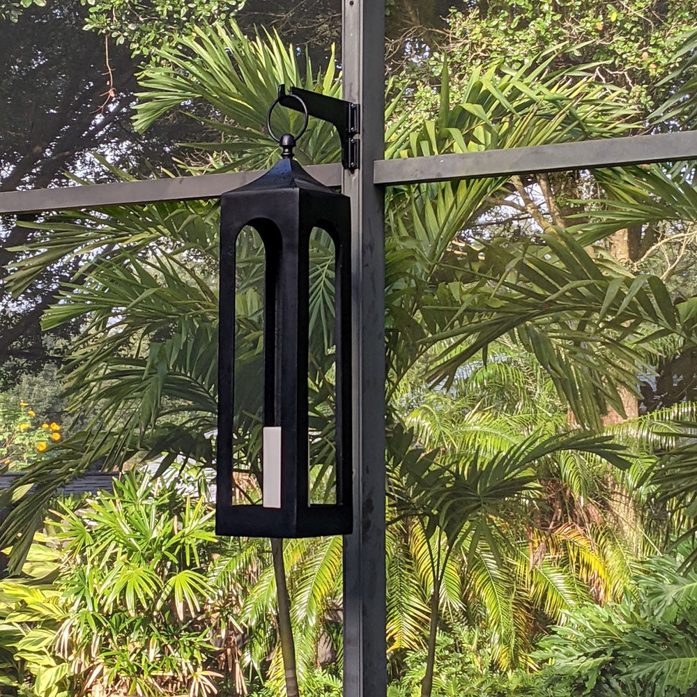 Outdoor lantern hanging on metal stand with greenery.