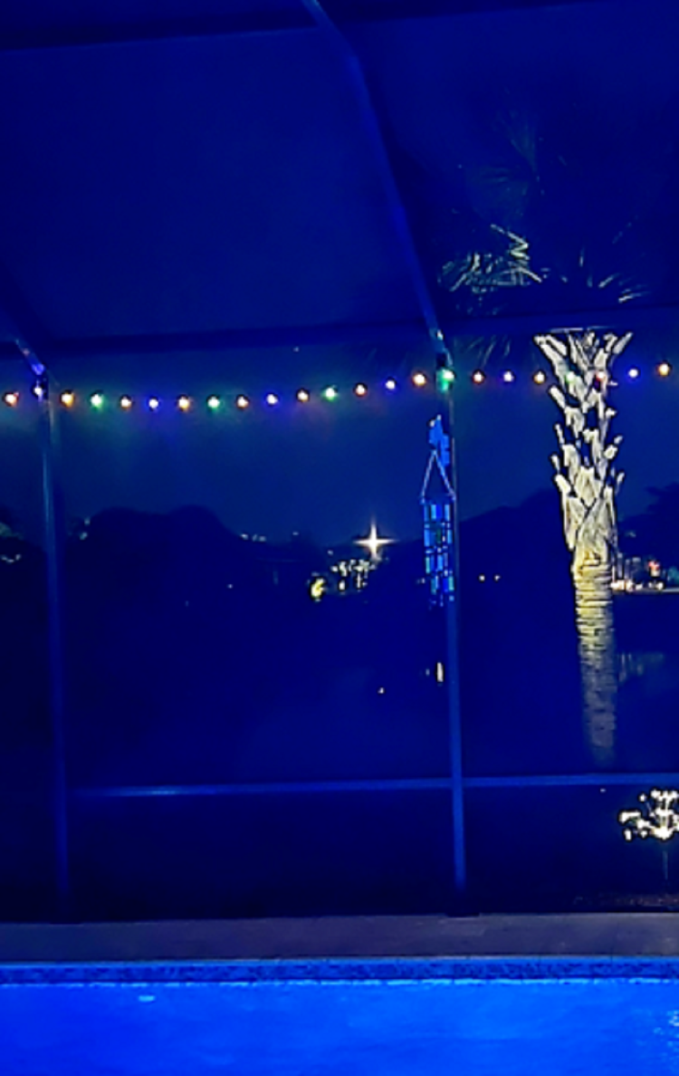 String lights over a lit pool in a screened lanai at night.