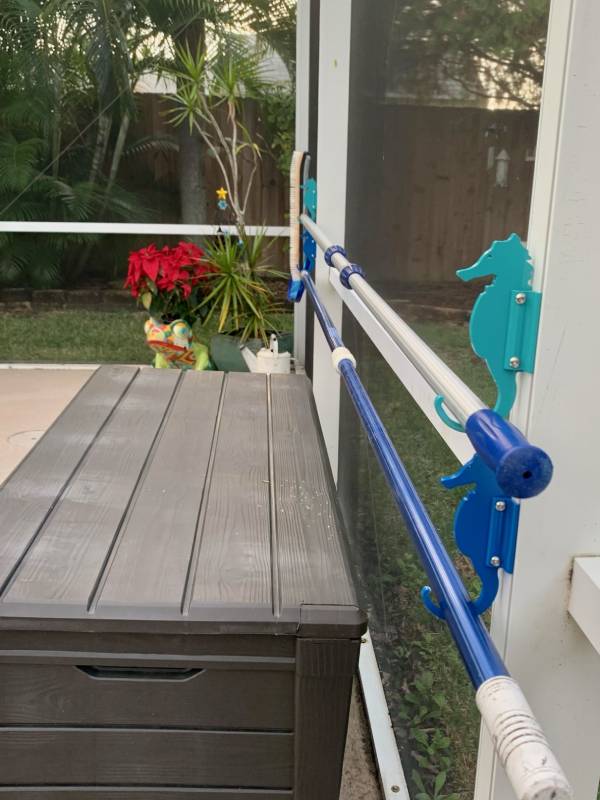 Teal seahorse hooks holding a blue pool pole above storage box.