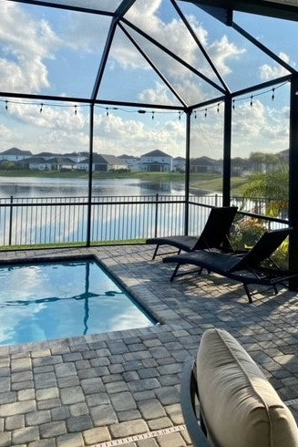 Modern pool cage with pool, lounge chairs, lake and string lights.