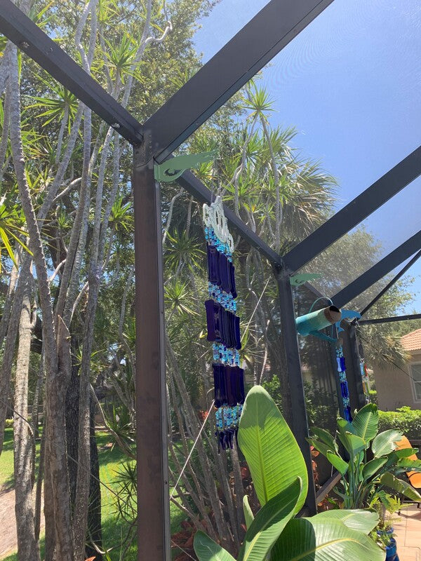 Wind chime on dark enclosure post among foliage.