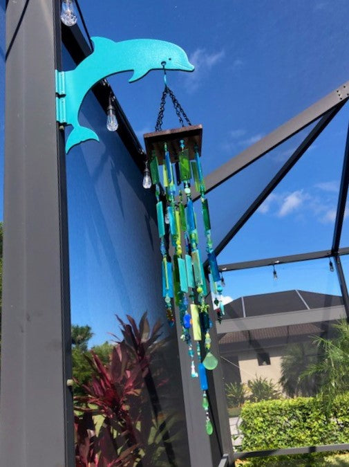 Teal dolphin hanger with wind chime on dark post.