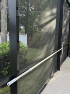 Black anchor hooks on dark screen-enclosure posts holding a long white pool pole across the posts.