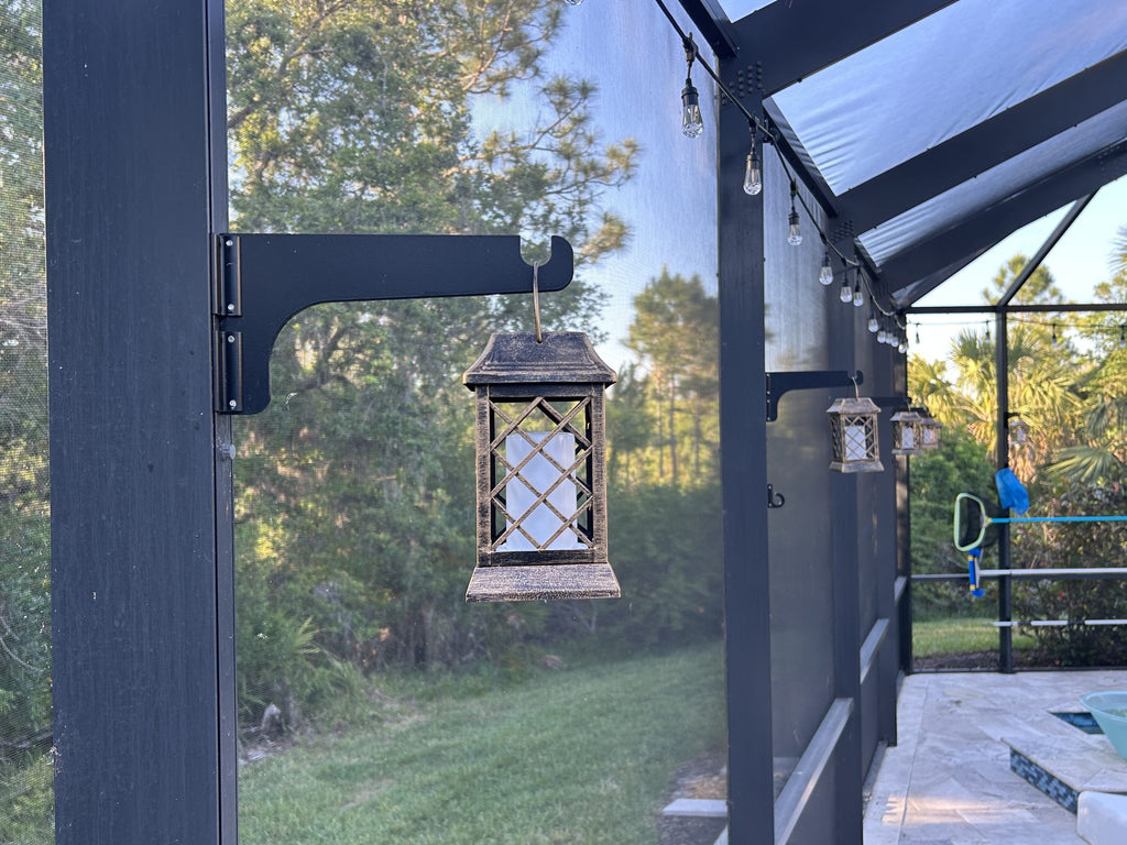 Black classic hanger on a dark lanai post holding a lantern beside a lawn.