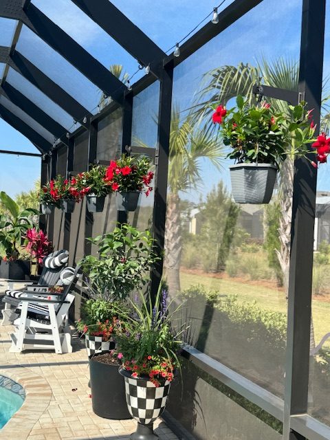 Black classic hangers on dark lanai posts holding red flower baskets above planters.