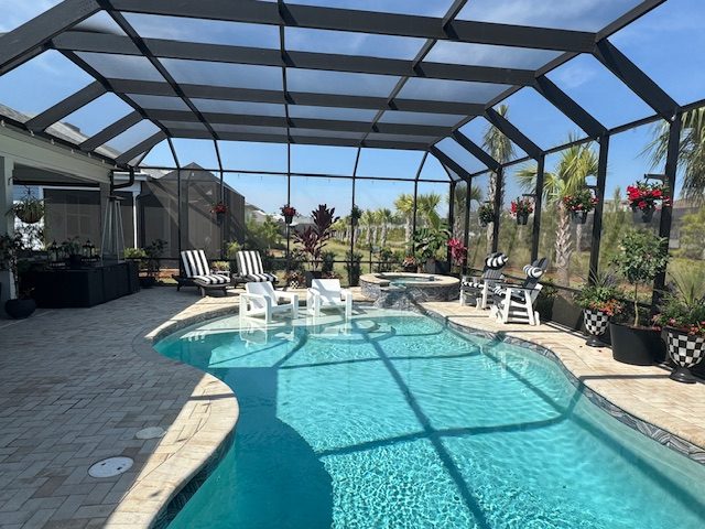 Wide view of a screened pool enclosure with hanging flower baskets on black hangers around the pool.