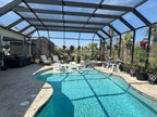 Wide view of a screened pool enclosure with hanging flower baskets on black hangers around the pool.