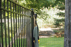 Black large classic hook on a black aluminum fence post holding a coiled garden hose by a gate.