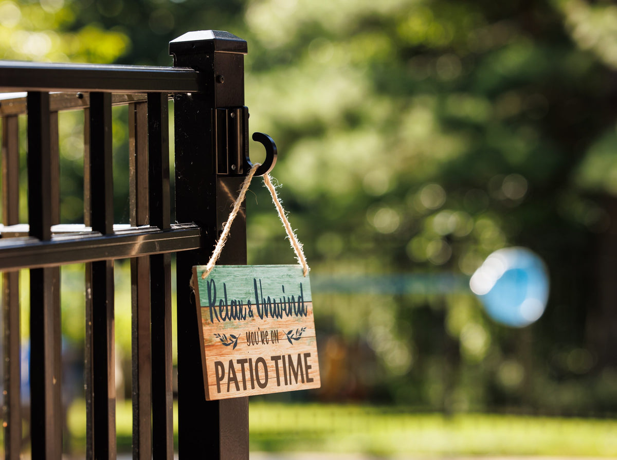 Black classic loop hook on a black aluminum fence post holding a Relax and Unwind sign.