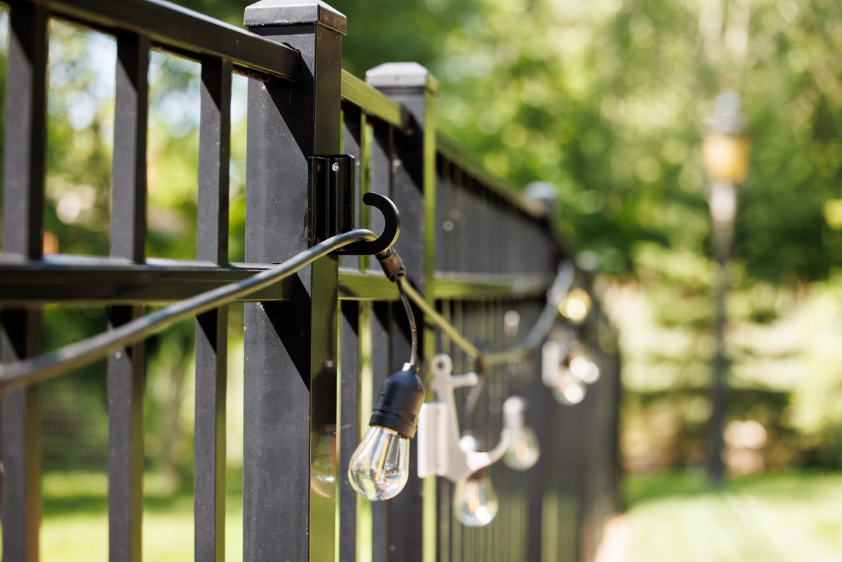 Black classic loop hooks on black aluminum fence posts holding a strand of string lights.