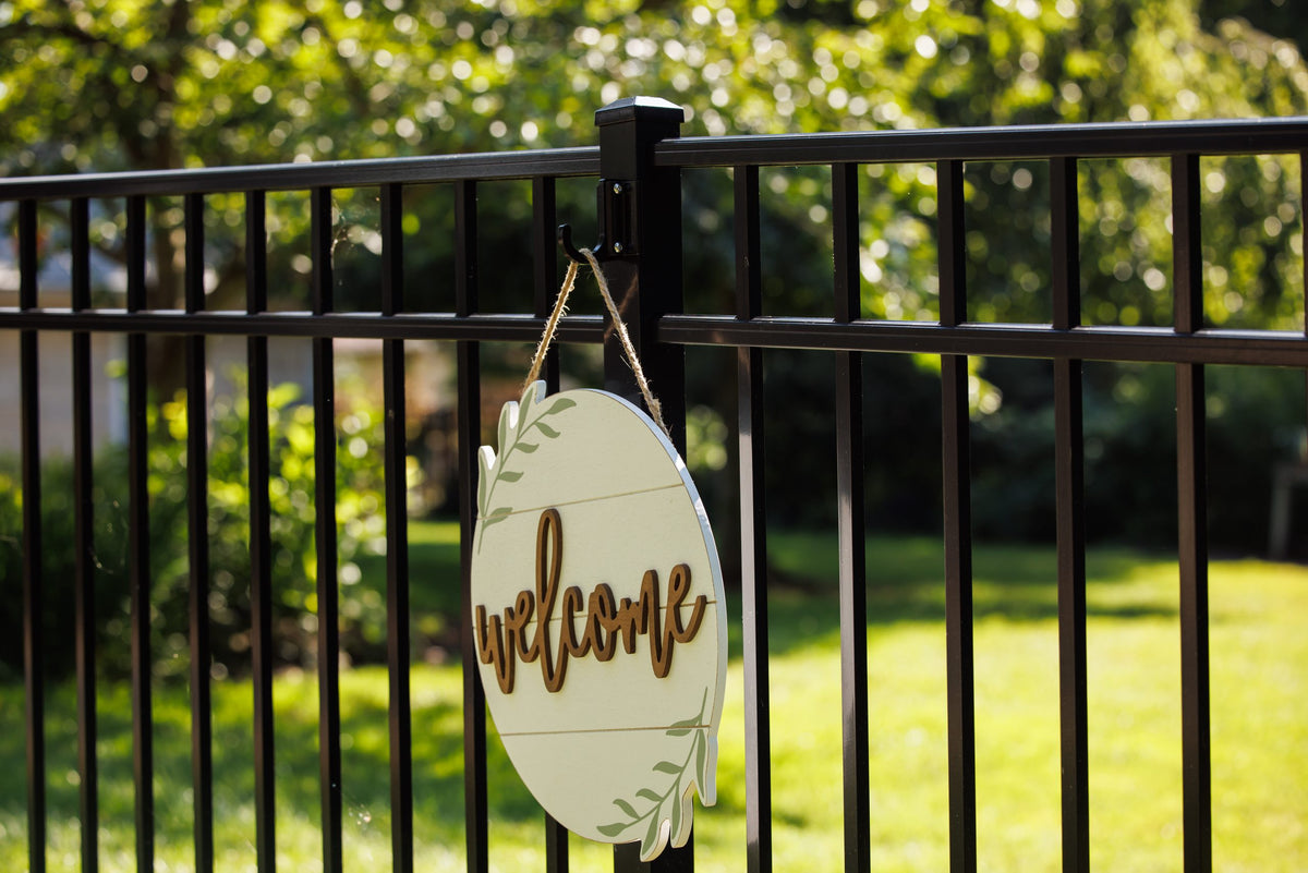 Black medium classic hook on a black aluminum fence post holding a round wooden welcome sign.