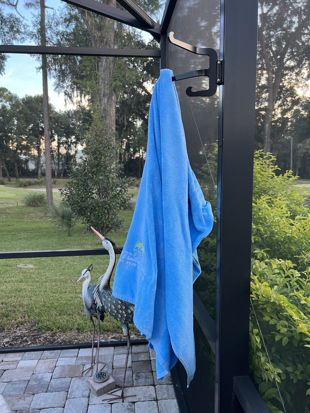 Black classic triple hook on a dark lanai post holding a blue towel, a heron statue below.