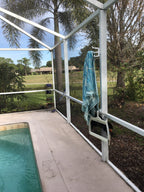 White classic triple hook on a white pool-cage post holding a teal towel beside the pool.