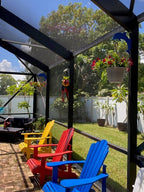 Blue dolphin hanger on a dark lanai post holding red flowers above colorful Adirondack chairs.