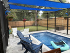 Pool enclosure with blue shade sails, dolphin hangers holding flower baskets and a wood fence.