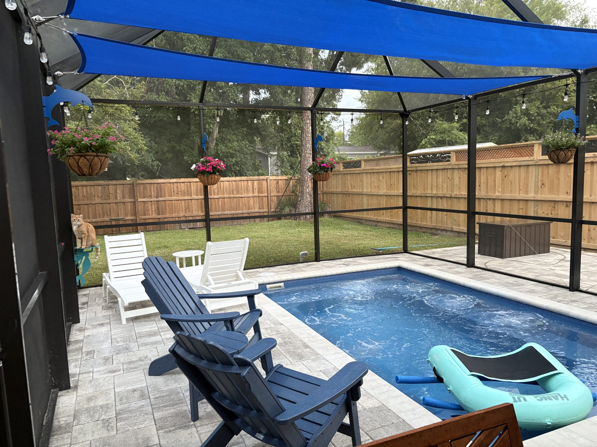 Pool enclosure with blue shade sails, dolphin hangers holding flower baskets and a wood fence.