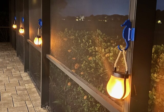 Blue seahorse hooks on dark lanai posts each holding a glowing lantern at night.