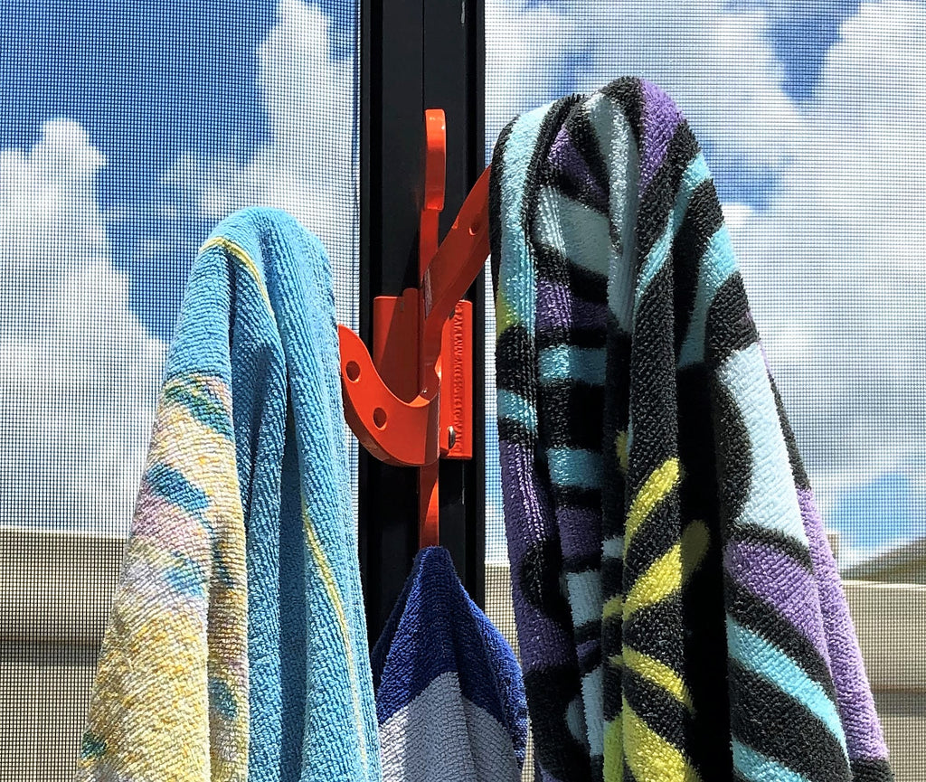 Close view of an orange octopus hook on a dark pool-cage post holding three striped beach towels.