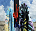 Close view of an orange octopus hook on a dark pool-cage post holding three striped beach towels.