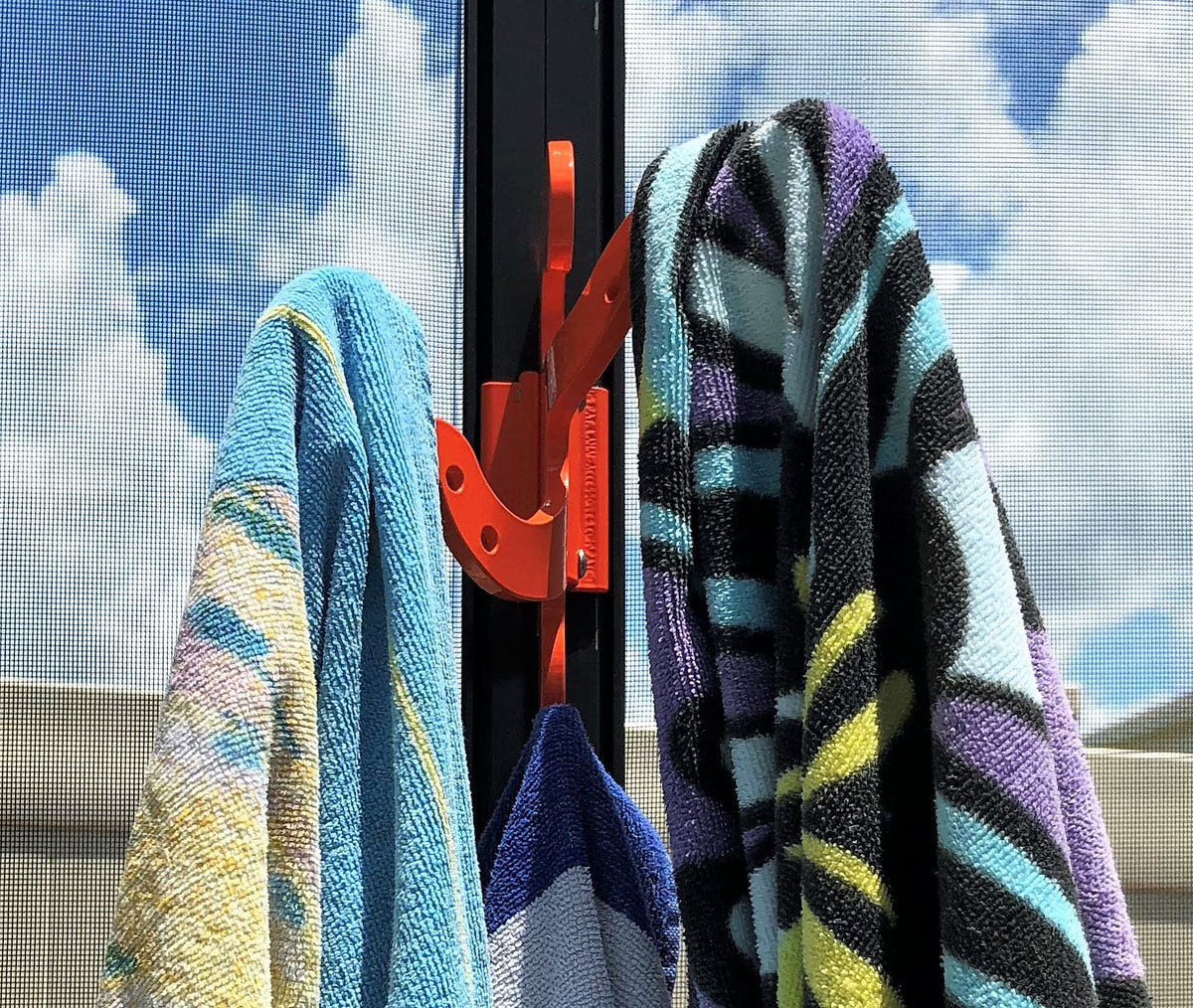 Close view of an orange octopus hook on a dark pool-cage post holding three striped beach towels.