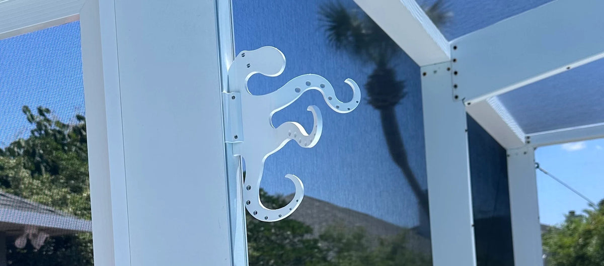 White octopus hook clamped to a white pool-cage post under blue sky and palm trees.