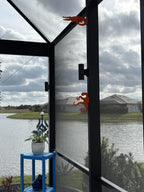 Two orange octopus hooks on dark screen-enclosure posts overlooking a lake, a blue plant stand below.