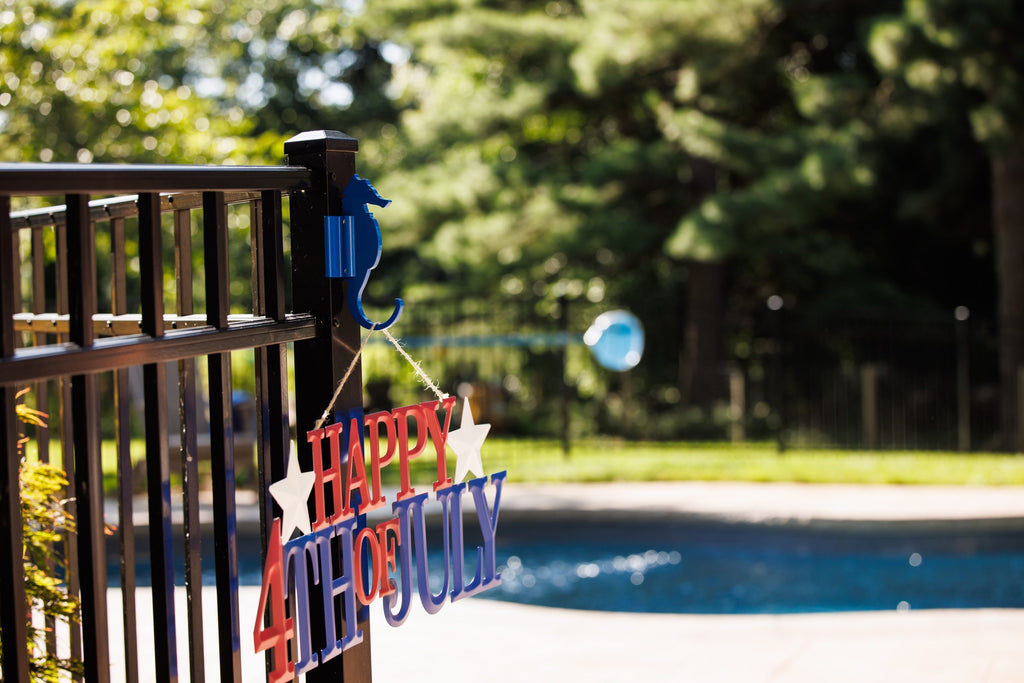 Blue seahorse hook on a black aluminum fence post holding a Happy 4th of July sign.