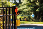 Orange seahorse hook on a black aluminum fence post holding a yellow lantern near a pool.