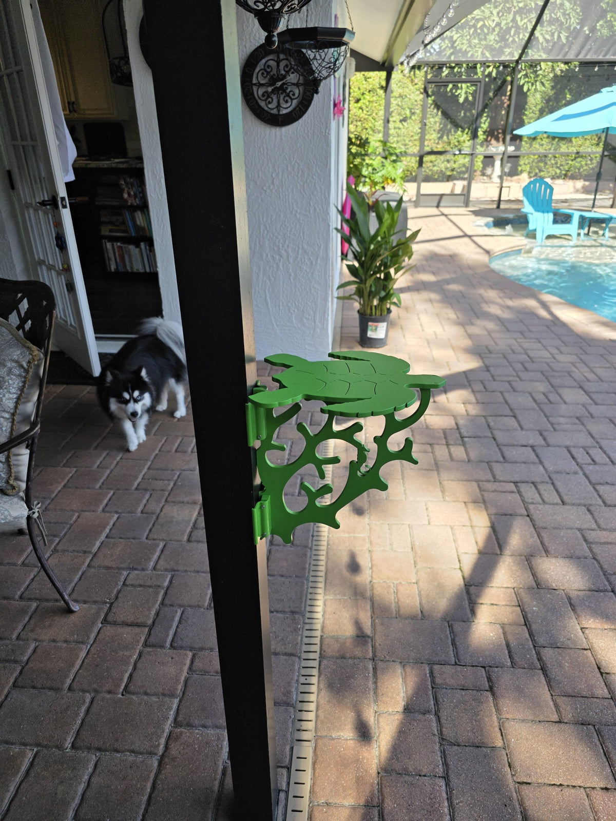 Lime green turtle mini table clamped to a dark lanai post on a brick paver patio.