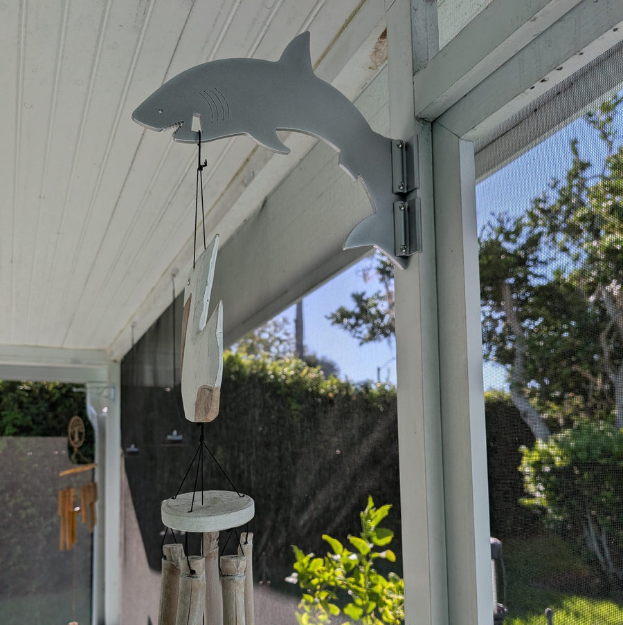 Grey shark hanger with a wind chime on a covered patio.