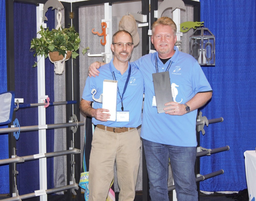 Two men holding brochures at trade-show booth with hooks on display.