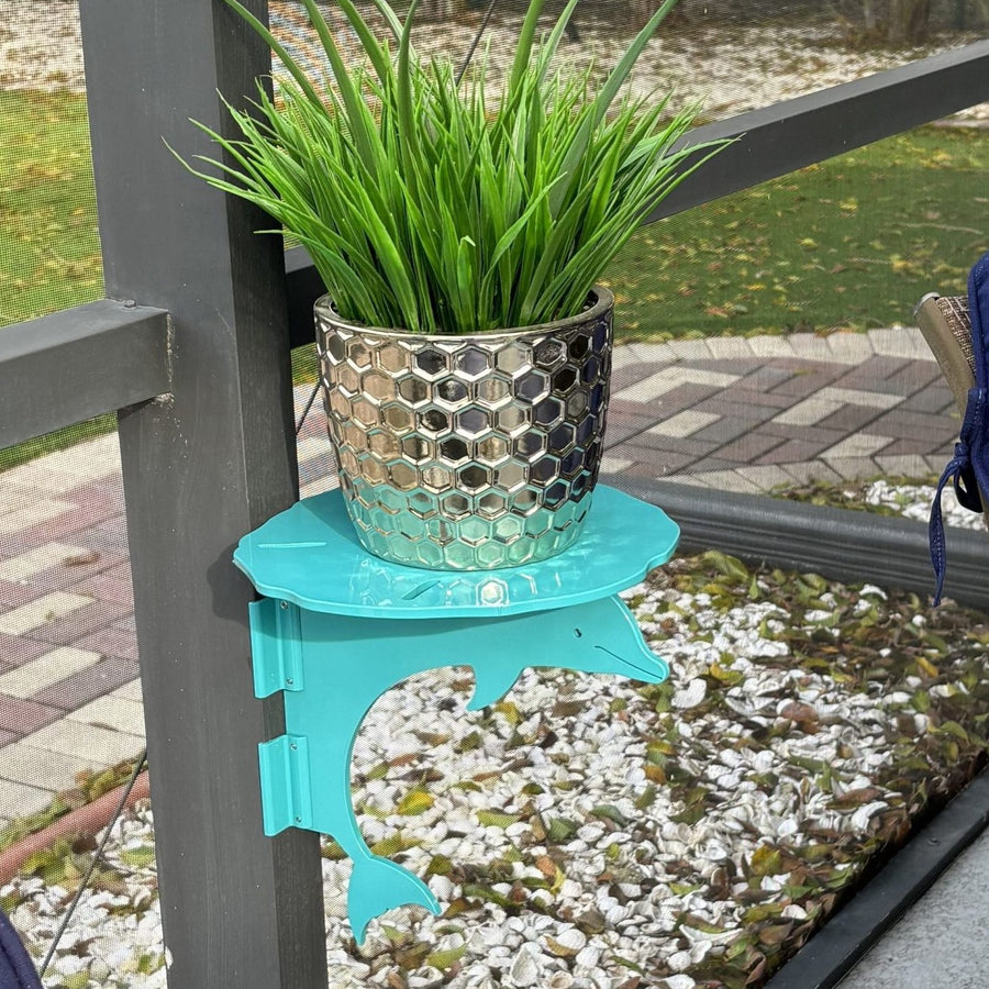 Teal dolphin mini table on dark post holding potted grass.